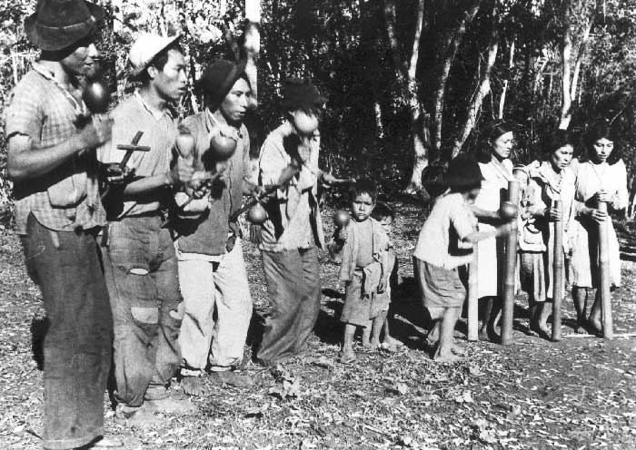 Kaiowa entre instrumentos tradicionais guarani e uma cruz do cristianismo. Foto: Egon Shaden, 1949.