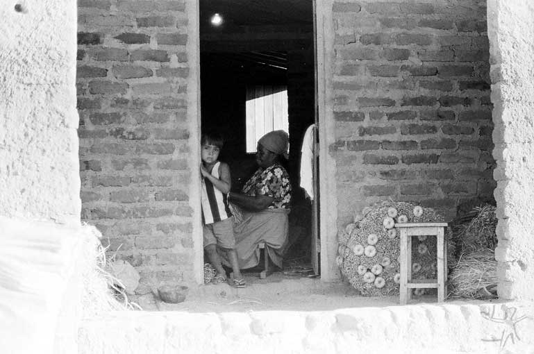 Avó e neta na sala de casa durante a produção de vassouras de palha de buriti. Foto: José Maurício Arruti, 1994.