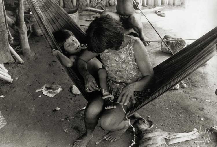 Mulher tecendo tornozeleira em seu filho. Foto: Antônio Carlos Moura, s/d.